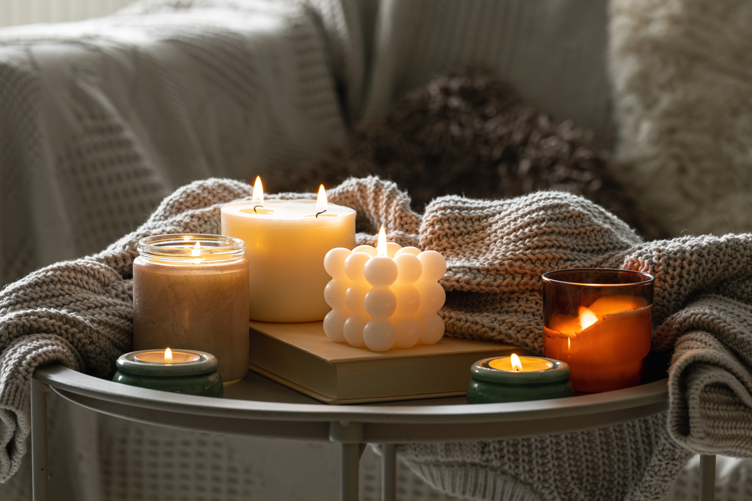 Cozy still life with a set of burning candles and a knitted element on a blurred background of the interior of the room.